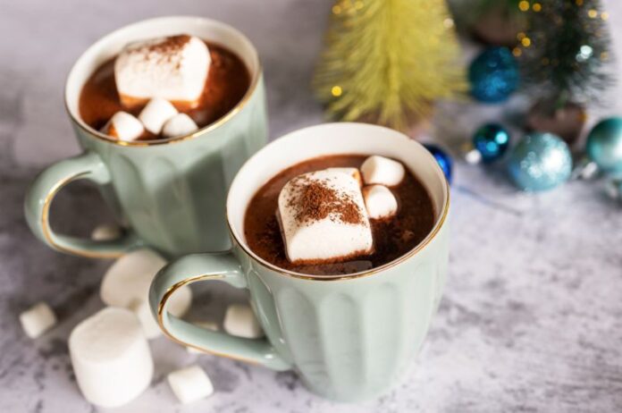 A steaming mug of hot chocolate topped with marshmallows, set on a wooden table with a cozy background.