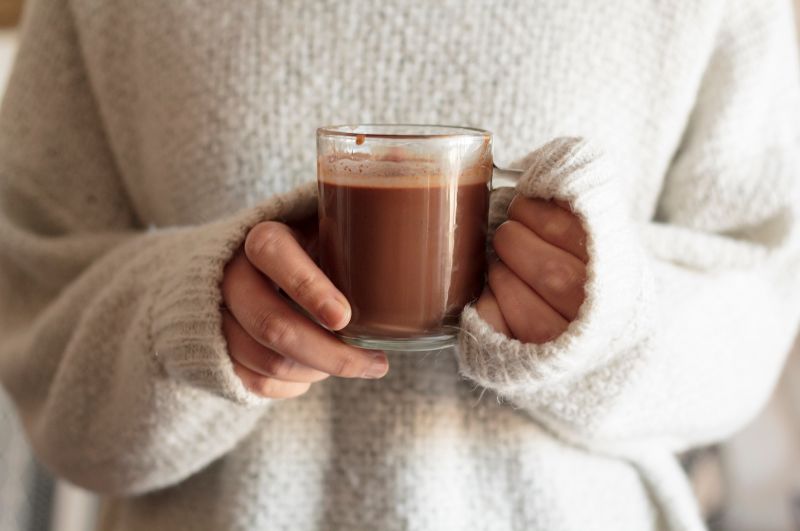 A cozy scene of a person enjoying a steaming cup of hot chocolate, surrounded by ingredients like cocoa powder and a variety of health-boosting spices.