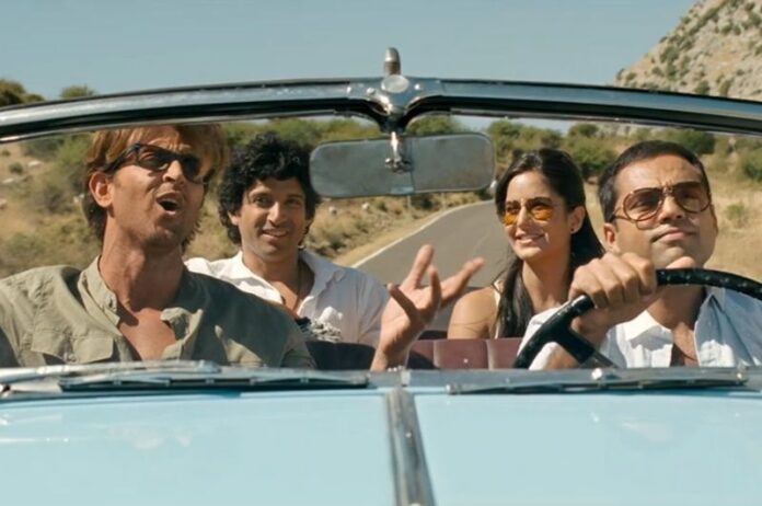 A group of friends enjoying a scenic road trip through a lush countryside landscape, with mountains in the background and a clear blue sky. Zindagi Na Milegi Dobara