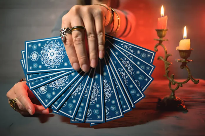 A hand holding a fanned-out deck of tarot cards with intricate blue and white designs, suggesting the practice of tarot readings for health insights